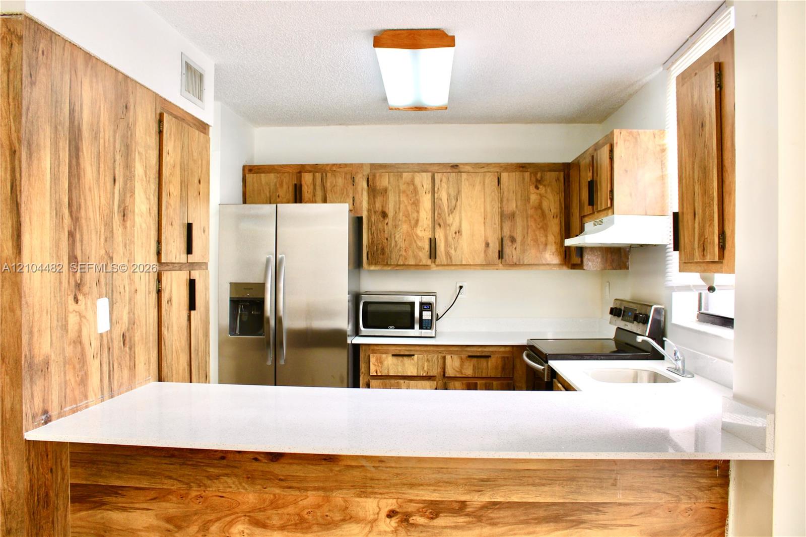 Kitchen featuringwhite solid-surface countertops, a stainless steel refrigerator, an integrated microwave, and an undermount sink