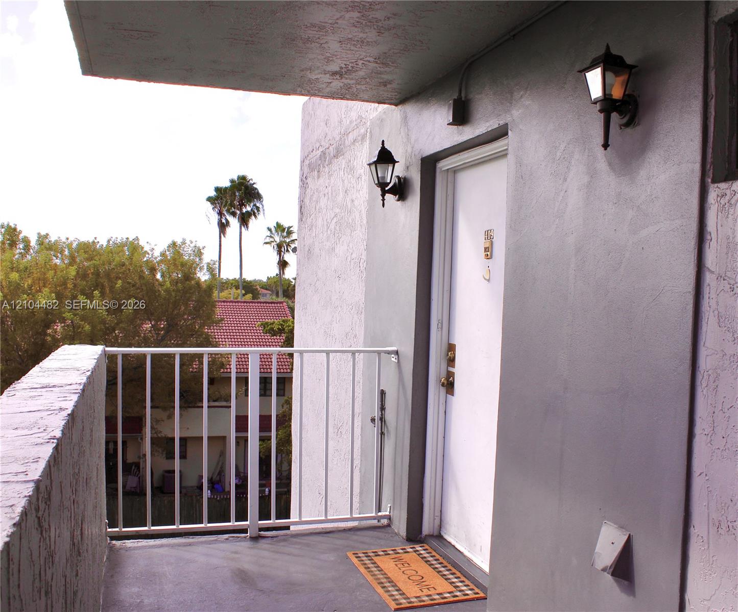Covered balcony entryway featuring a painted concrete surface, white metal railings, and dual wall-mounted exterior lanterns