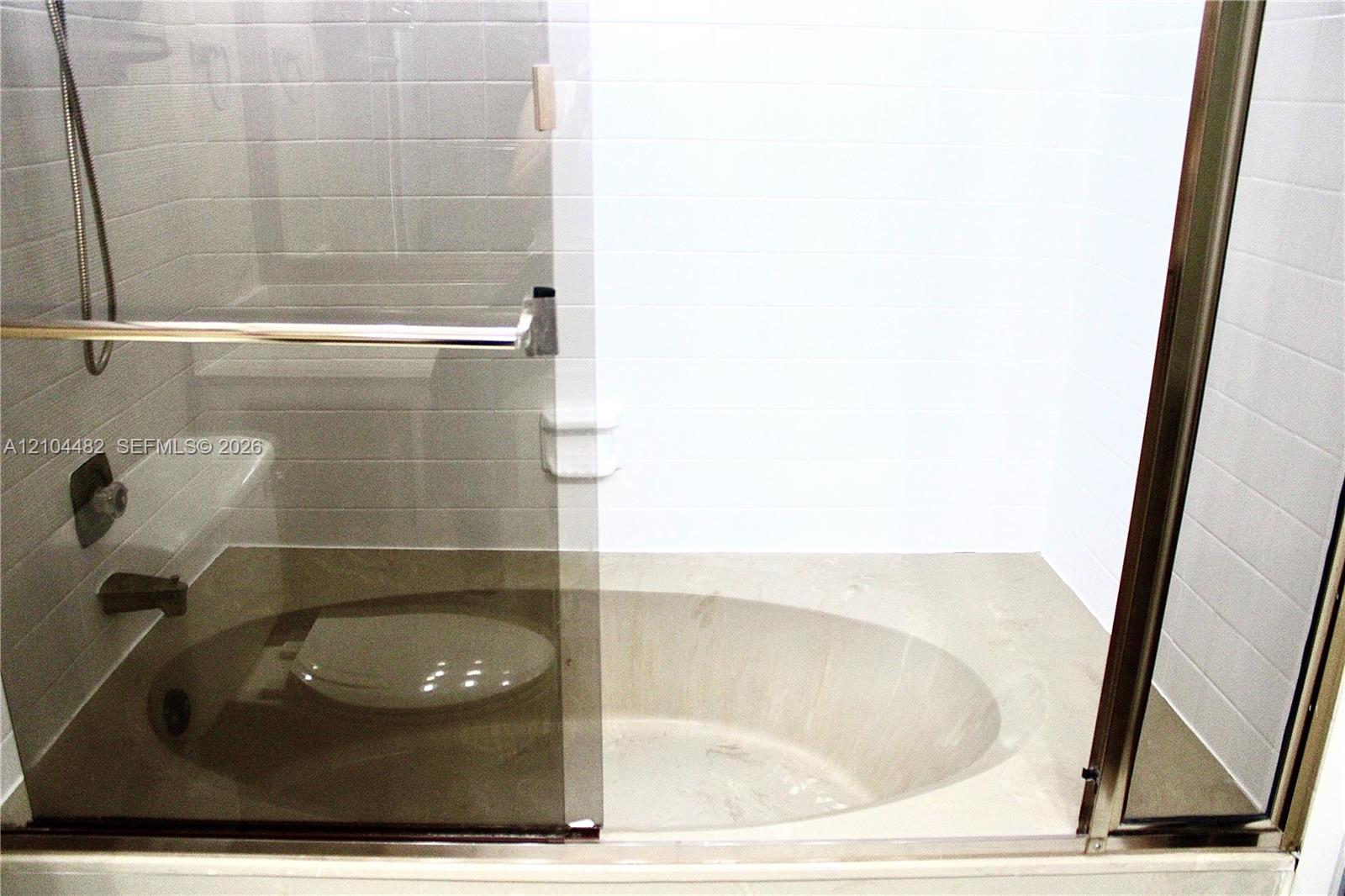 Built-in oval soaking tub with stone-finish surround, sliding glass enclosure, white ceramic wall tile, and metallic hardware