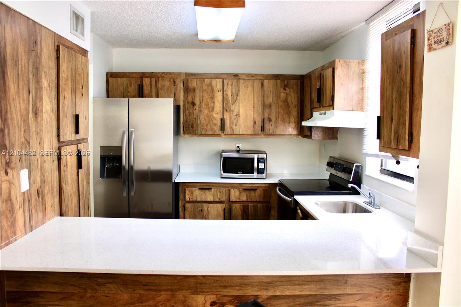 Kitchen featuring wood-finish cabinetry, white solid-surface countertops, a breakfast bar, and stainless steel appliances