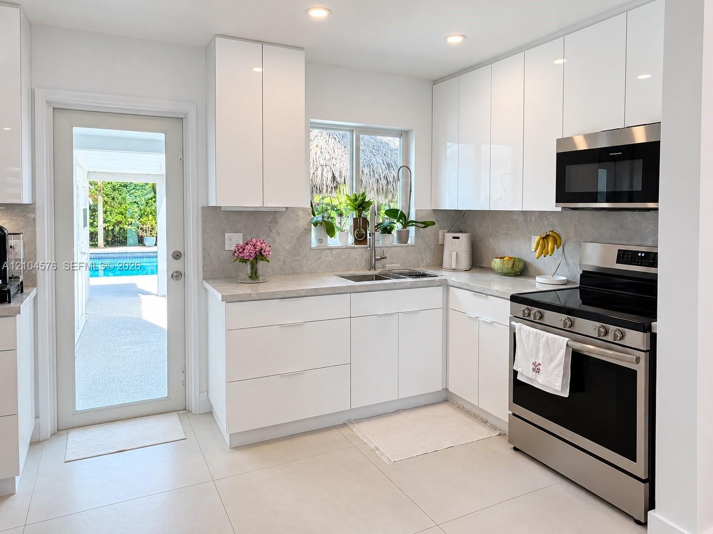 Kitchen featuring high-gloss white cabinetry, stone-finish countertops, stainless steel appliances, recessed ceiling lighting, and a glass-paneled exterior door Kitchen featuring high-gloss white cabinetry, stone-finish countertops, stainless steel appliances, recessed ceiling lighting, and a glass-paneled exterior door