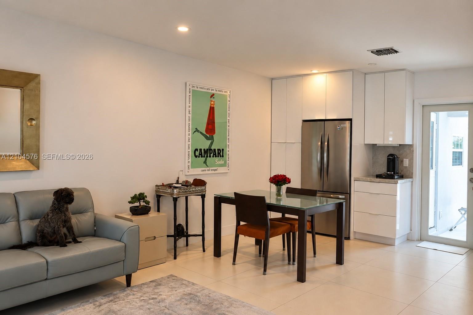 Contemporary interior featuring high-gloss white cabinetry, stainless steel refrigerator, large-format tile flooring, and recessed lighting Contemporary interior featuring high-gloss white cabinetry, stainless steel refrigerator, large-format tile flooring, and recessed lighting