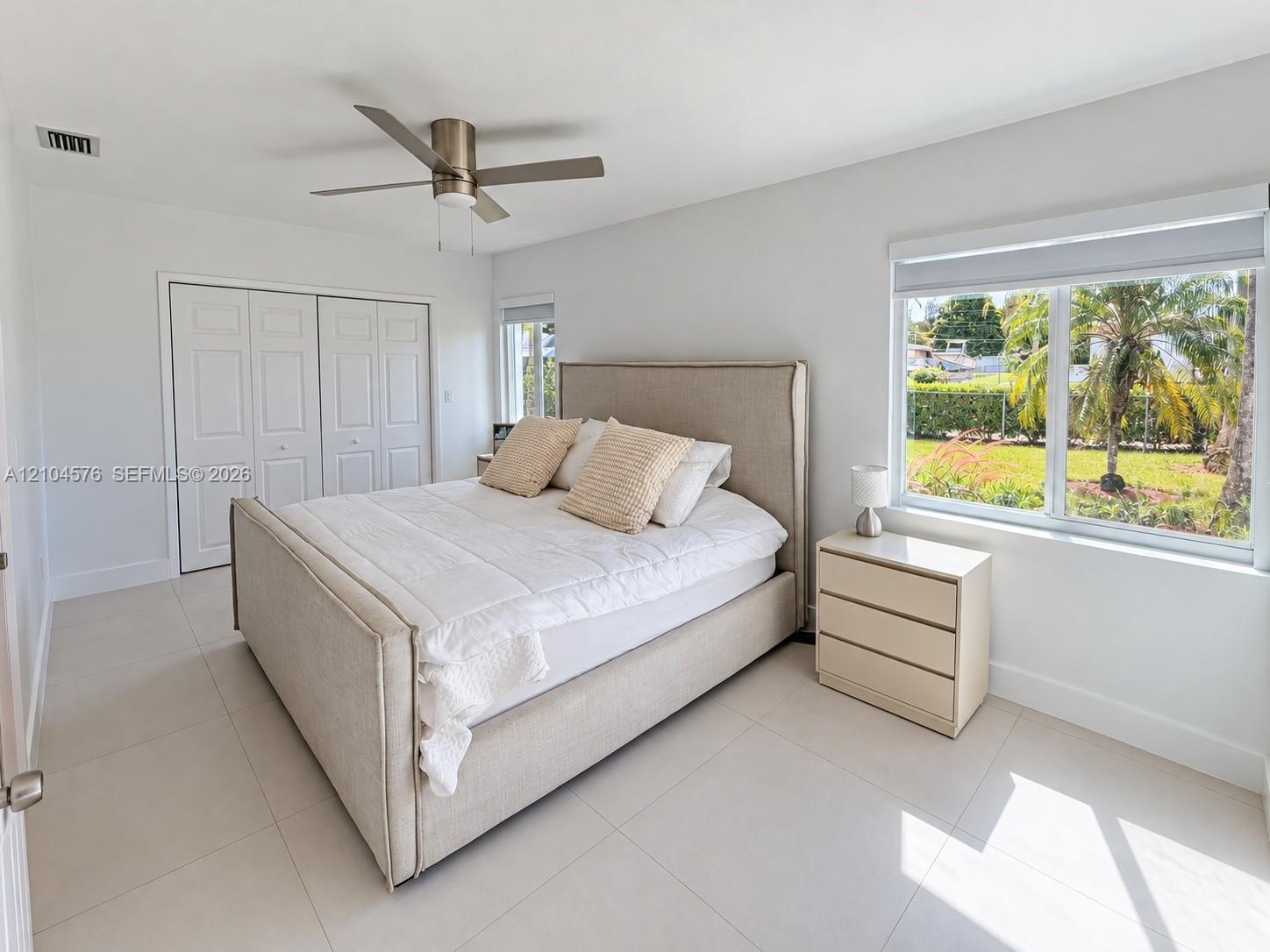 Neutral-toned ceramic tile flooring, dual-panel closet doors, ceiling fan with integrated lighting, and large windows providing natural illumination Neutral-toned ceramic tile flooring, dual-panel closet doors, ceiling fan with integrated lighting, and large windows providing natural illumination