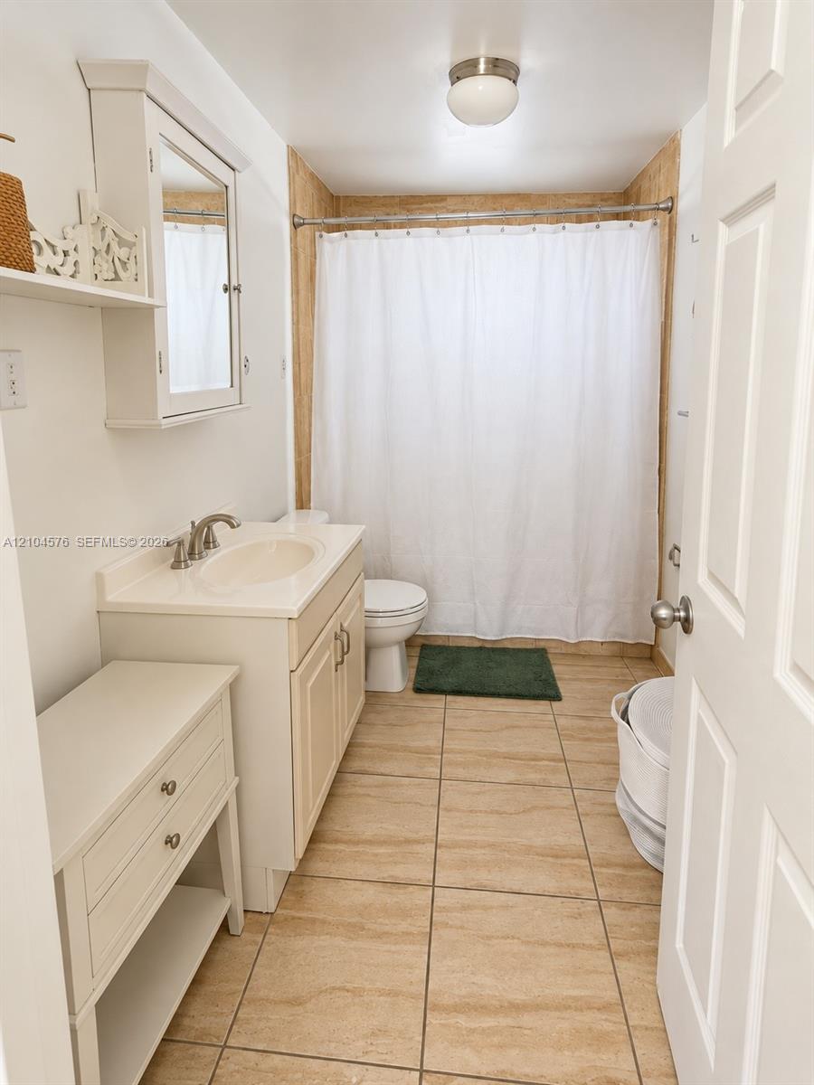 Bathroom featuring large-format stone-finish floor tiling, a white vanity cabinet with an integrated sink, a wall-mounted mirrored medicine cabinet, and a shower-tub combination with full-height tile surround