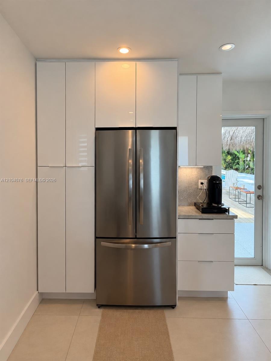 High-gloss white cabinetry, stainless steel French-door refrigerator, stone-surface countertop, recessed ceiling lighting, and large-format tile flooring High-gloss white cabinetry, stainless steel French-door refrigerator, stone-surface countertop, recessed ceiling lighting, and large-format tile flooring