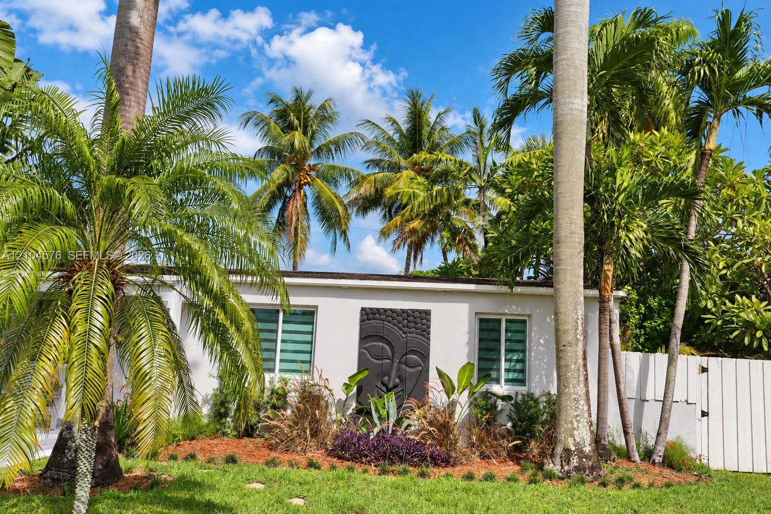 Exterior featuring white stucco facade, manicured landscaping with mature palm trees, decorative wall relief, and perimeter fencing Exterior featuring white stucco facade, manicured landscaping with mature palm trees, decorative wall relief, and perimeter fencing