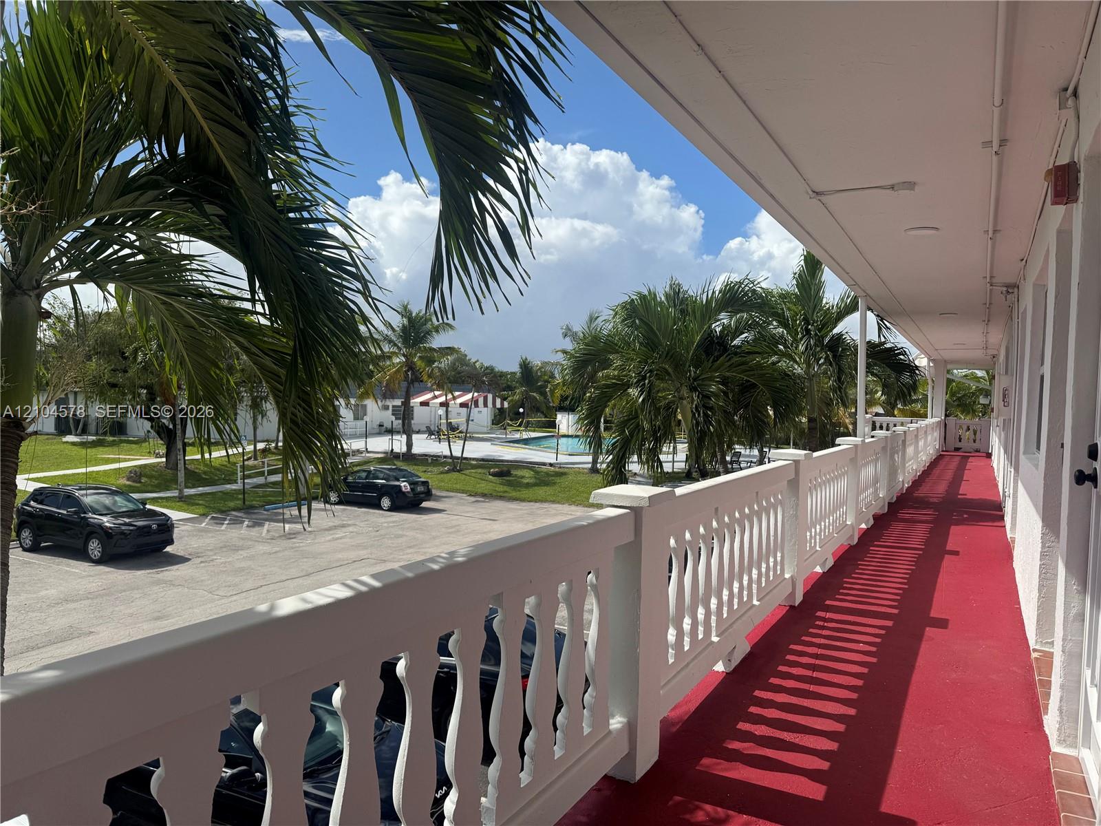 Covered exterior balcony featuring a white balustrade railing and crimson floor surfacing Covered exterior balcony featuring a white balustrade railing and crimson floor surfacing
