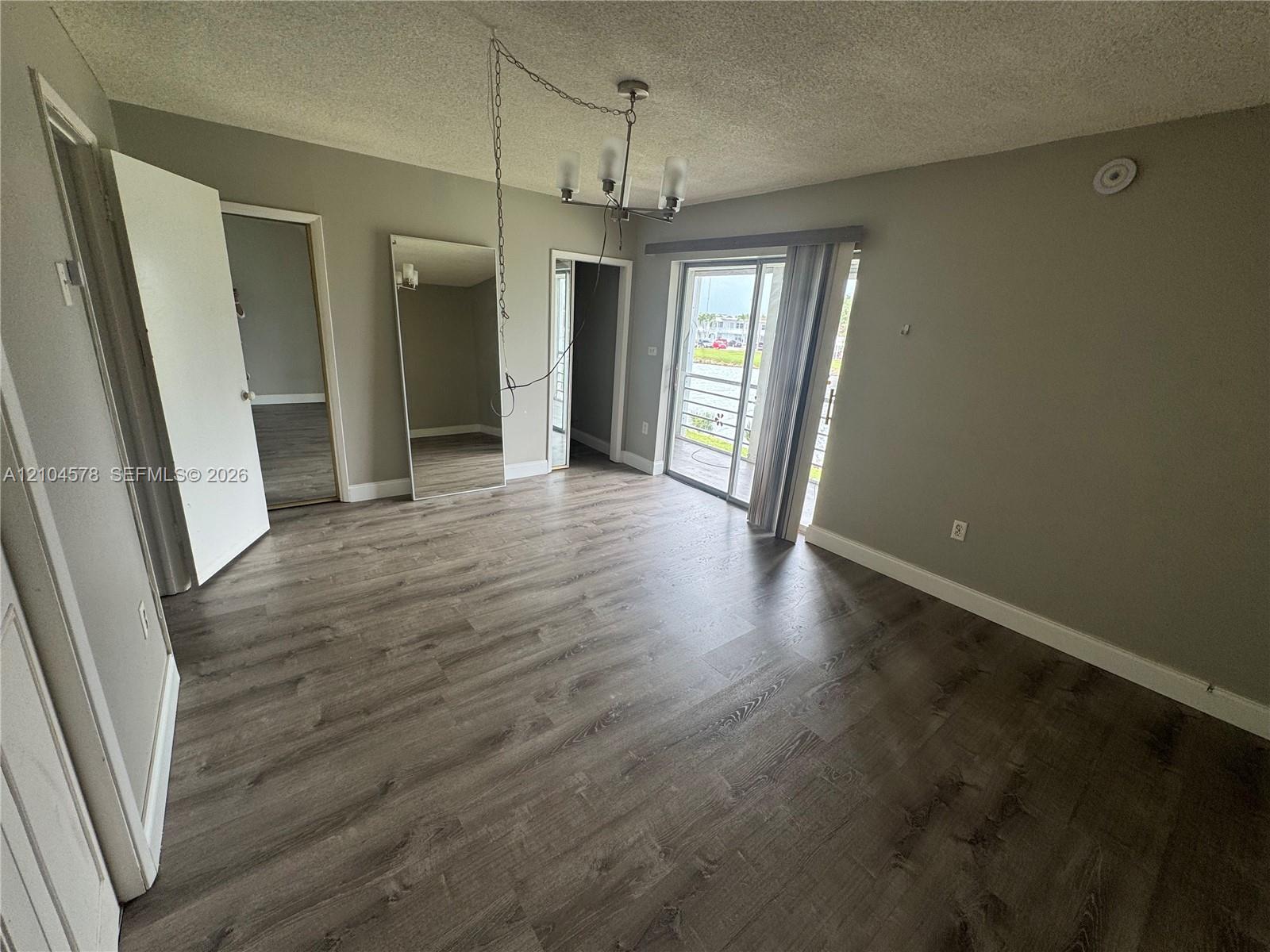 Interior space featuring wood-finish flooring, a full-length wall mirror, a hanging light fixture, and a sliding glass door providing external access