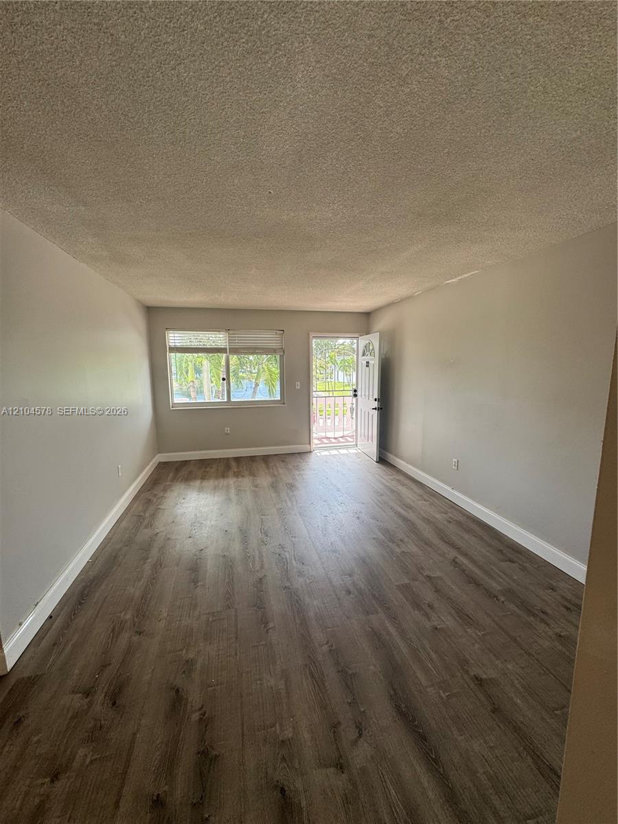 Interior space featuring wood-finish flooring, neutral wall paint, and natural light from a window and door Interior space featuring wood-finish flooring, neutral wall paint, and natural light from a window and door