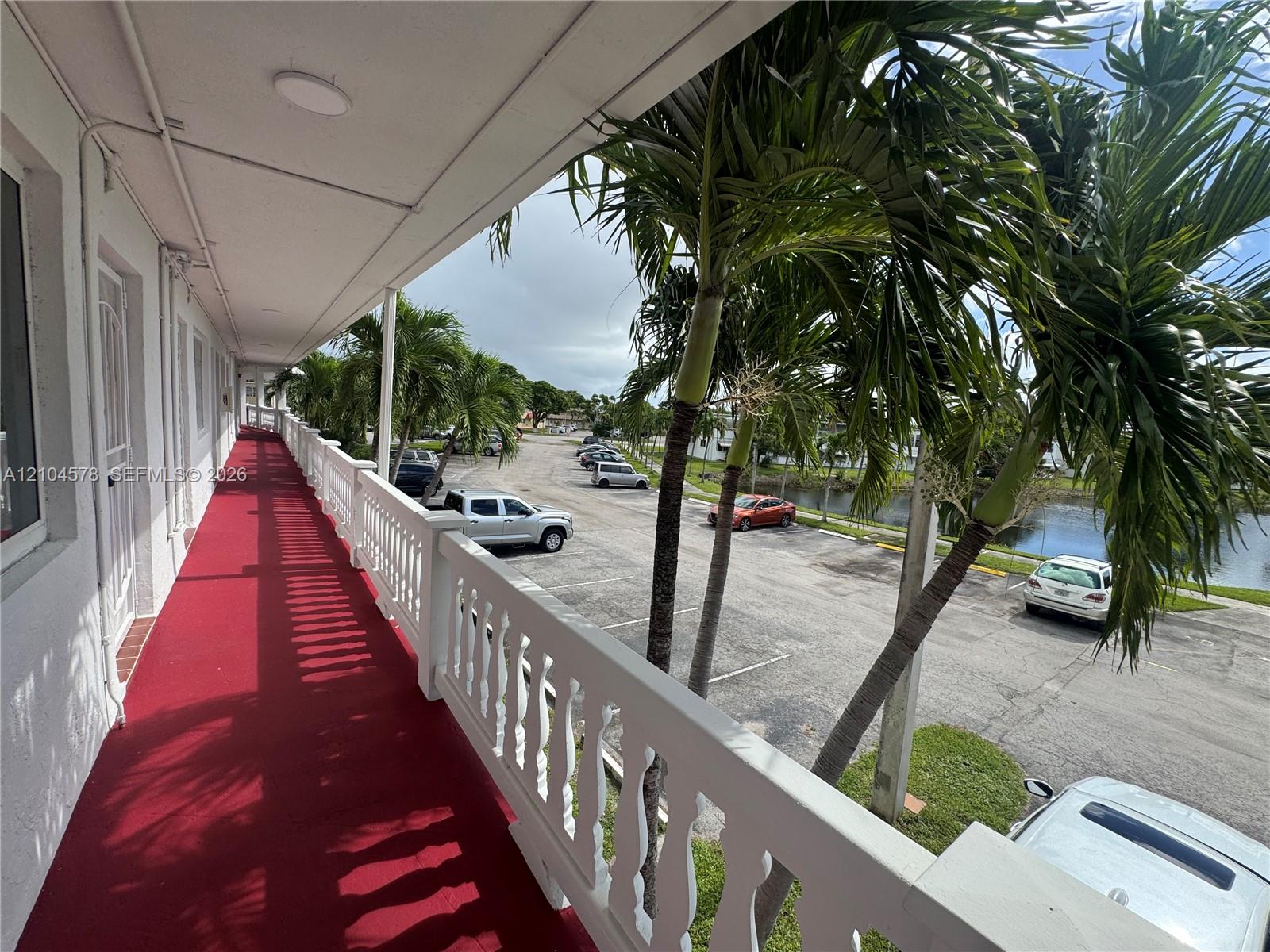 Covered exterior walkway featuring a red floor surface and a white balustrade railing Covered exterior walkway featuring a red floor surface and a white balustrade railing