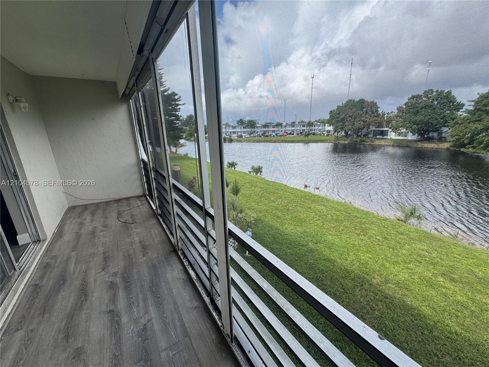 Screened-in balcony featuring wood-finish flooring, metal railing, and direct water frontage