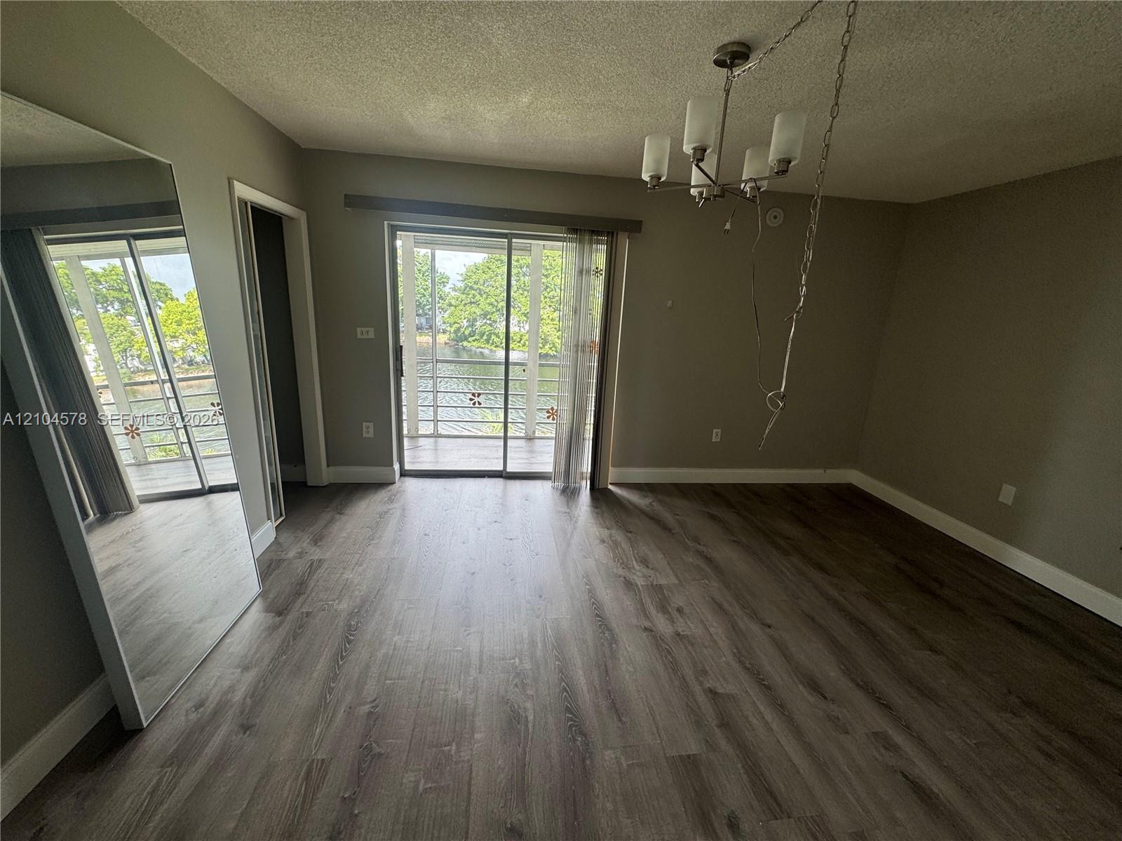 Wood-finish flooring, full-length mirrored wall panels, multi-arm chandelier with glass shades, and sliding glass doors opening to a screened balcony