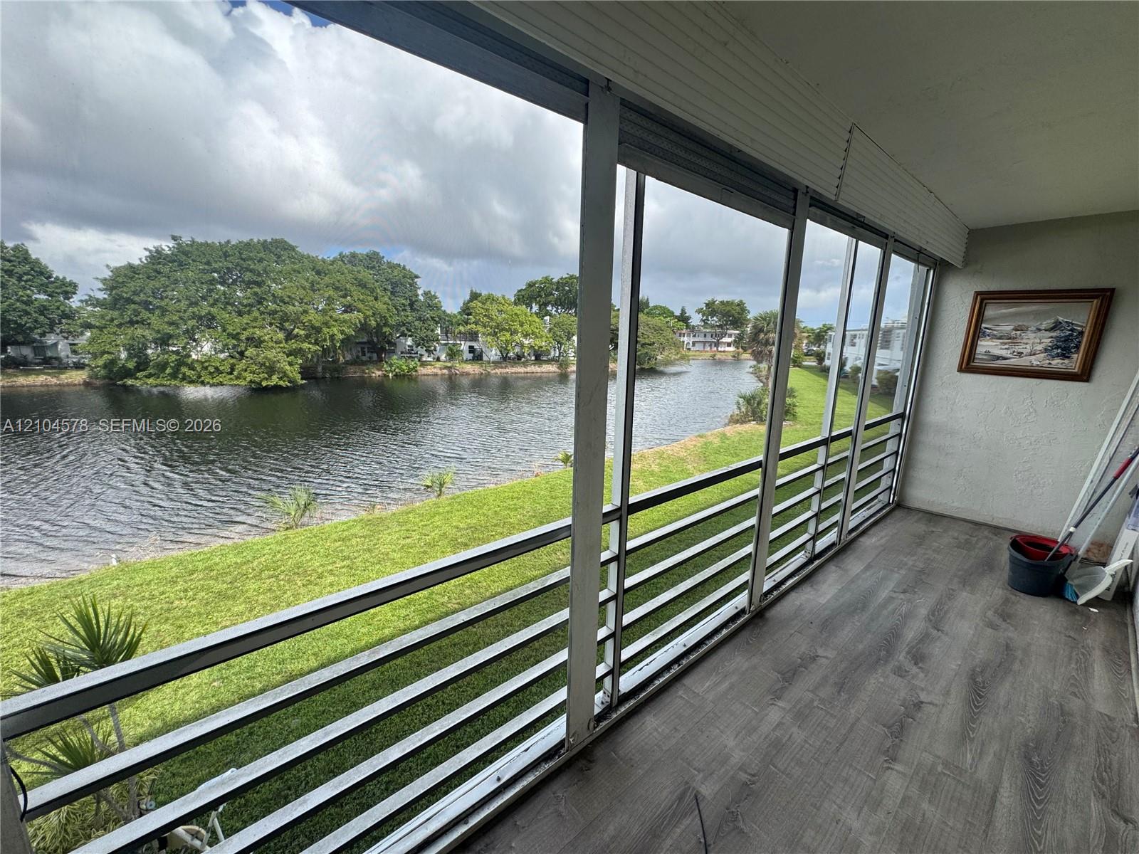 Screened-in porch featuring horizontal metal railings, wood-finish flooring, and direct exposure to a water canal