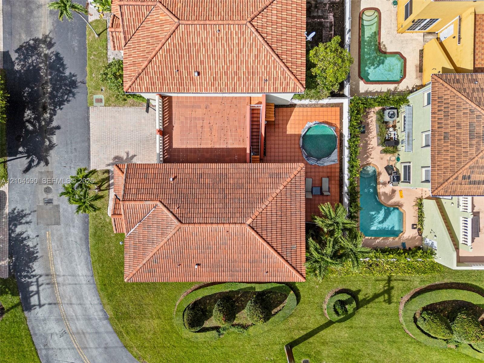Aerial perspective featuring a tile roof, paved driveway, brick-paver patio, and mature landscaping