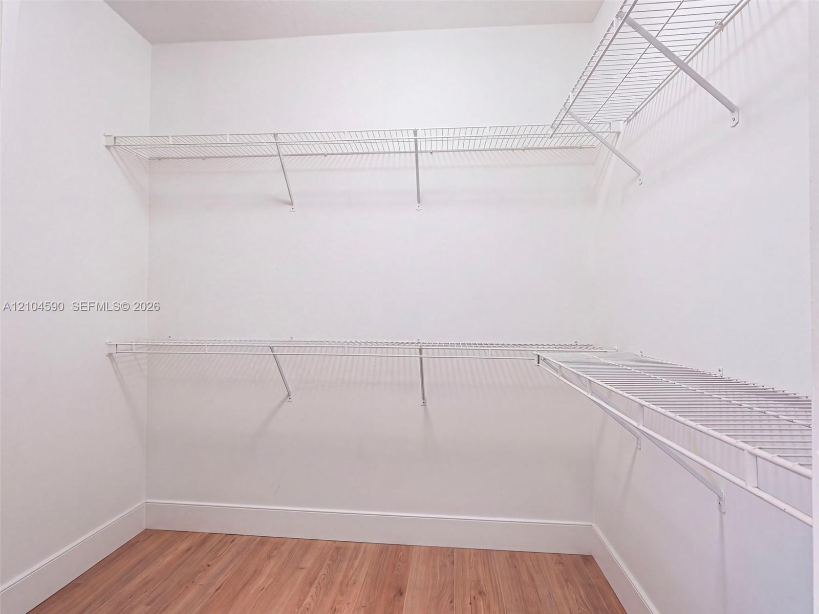 Walk-in closet featuring wood-finish flooring and tiered white wire shelving Walk-in closet featuring wood-finish flooring and tiered white wire shelving