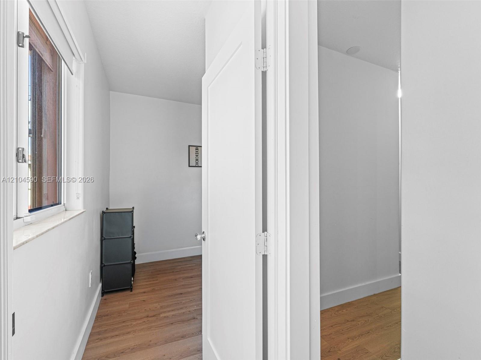 Neutral-toned walls paired with wood-finish flooring, a casement window featuring a stone-style sill, and a white interior door with brushed metal hardware