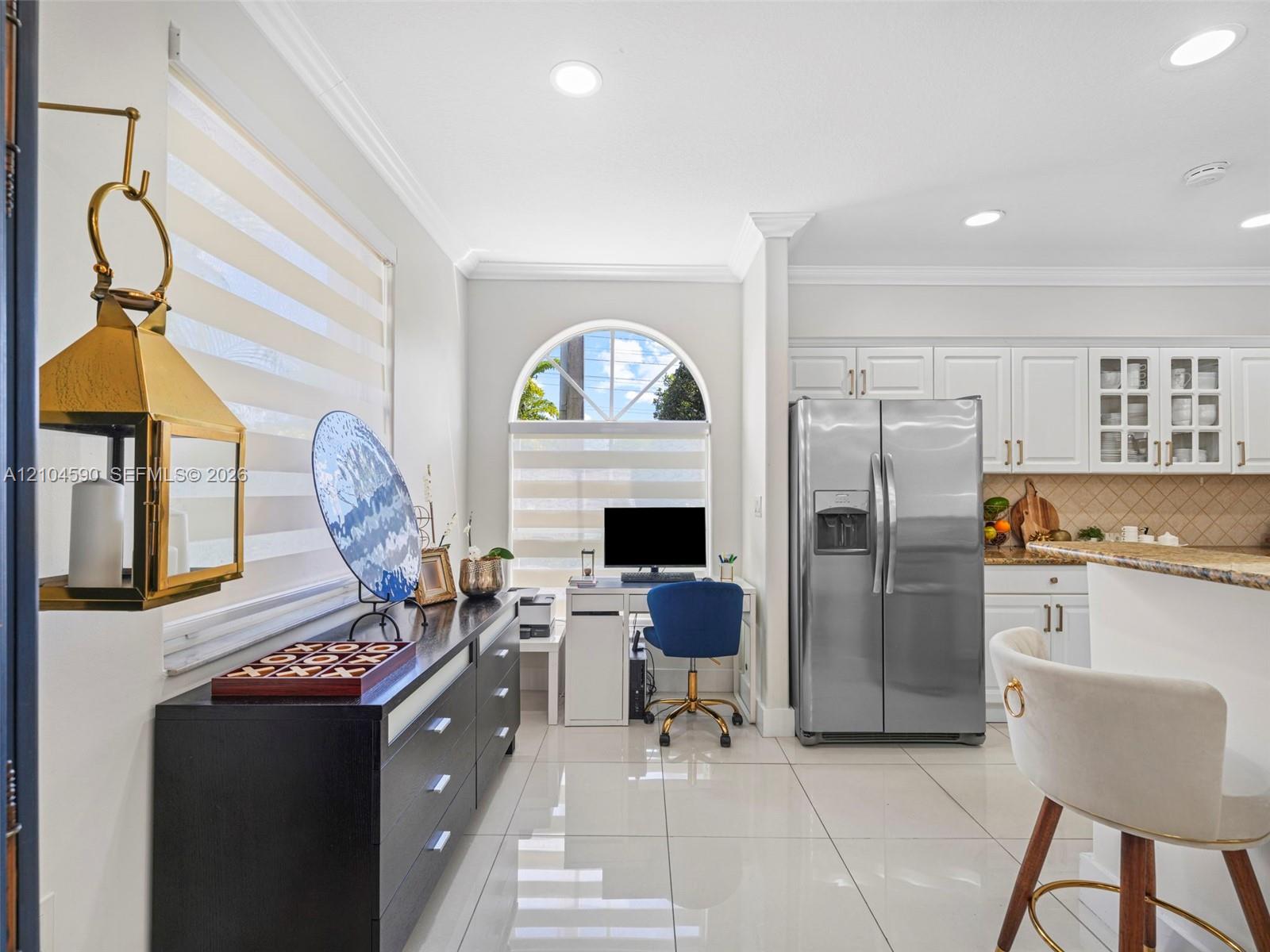 Kitchen featuring white cabinetry with glass-front uppers, stainless steel refrigerator, stone countertops, arched window, and large-format porcelain tile flooring