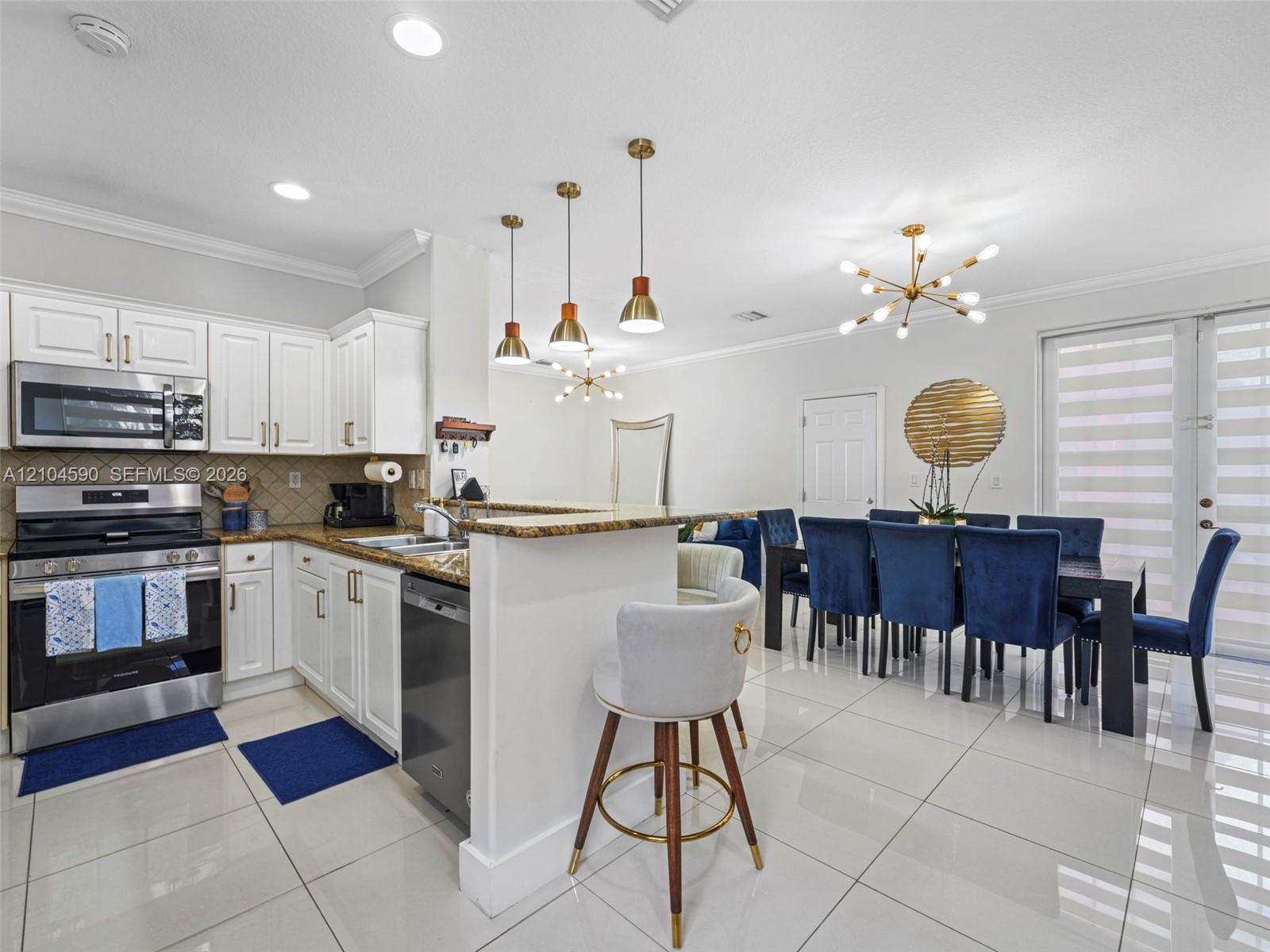 Kitchen featuring white cabinetry, stone countertops, stainless steel appliances, tiered pendant lighting, and polished floor tile Kitchen featuring white cabinetry, stone countertops, stainless steel appliances, tiered pendant lighting, and polished floor tile