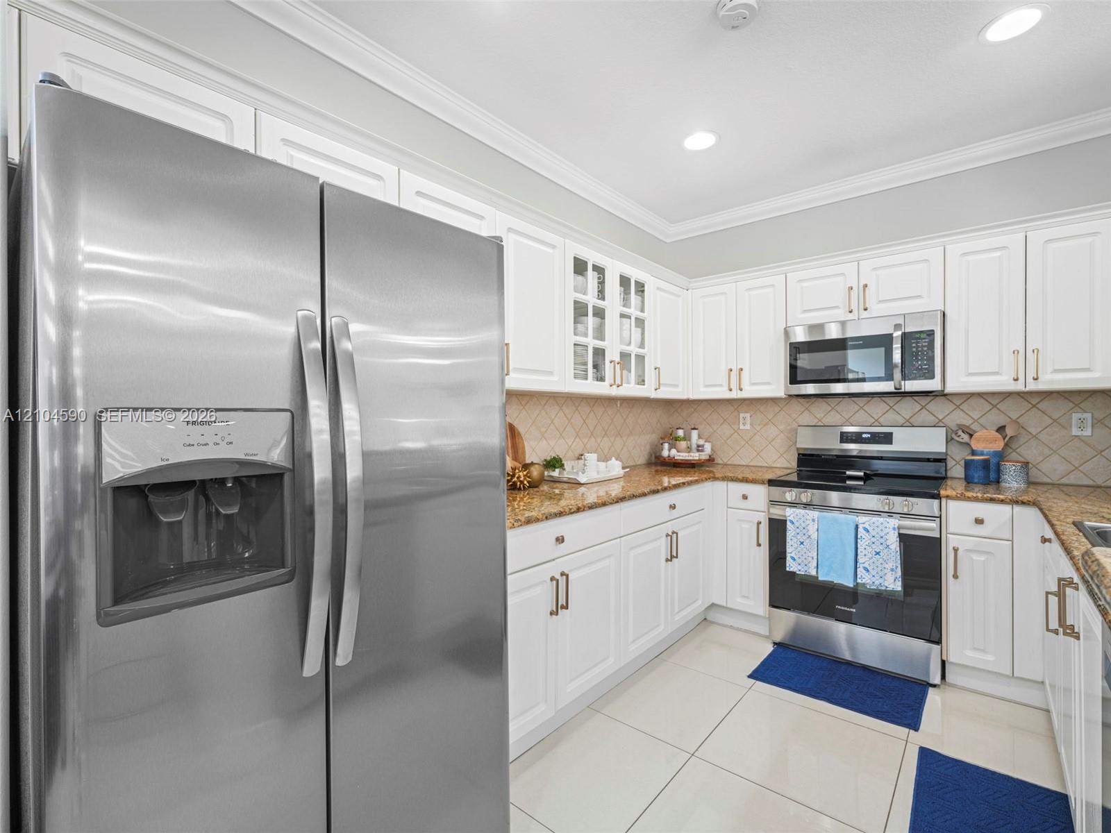 Kitchen featuring white cabinetry, stone countertops, stainless steel appliances, glass-front upper cabinet doors, and tile flooring