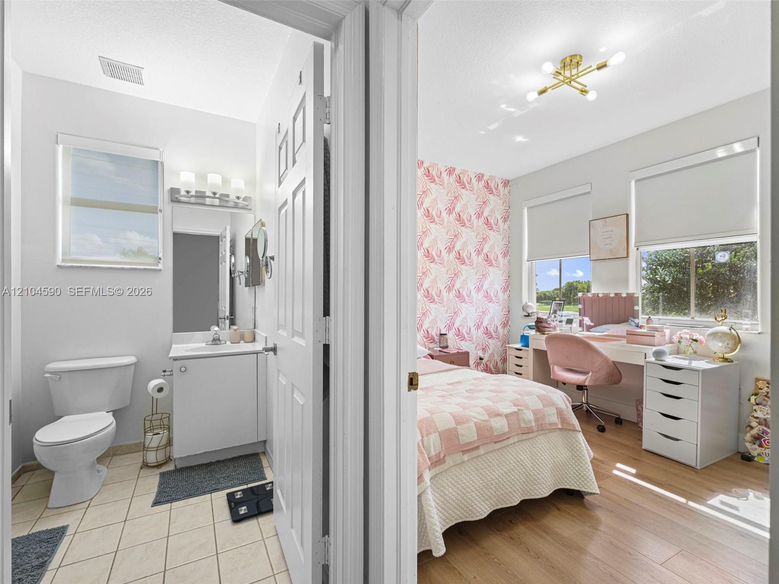 Bathroom featuring a white vanity with an integrated sink, three-light fixture, and ceramic tile flooring, paired with a bedroom showcasing wood-finish flooring, a multi-arm modern light fixture, and large windows