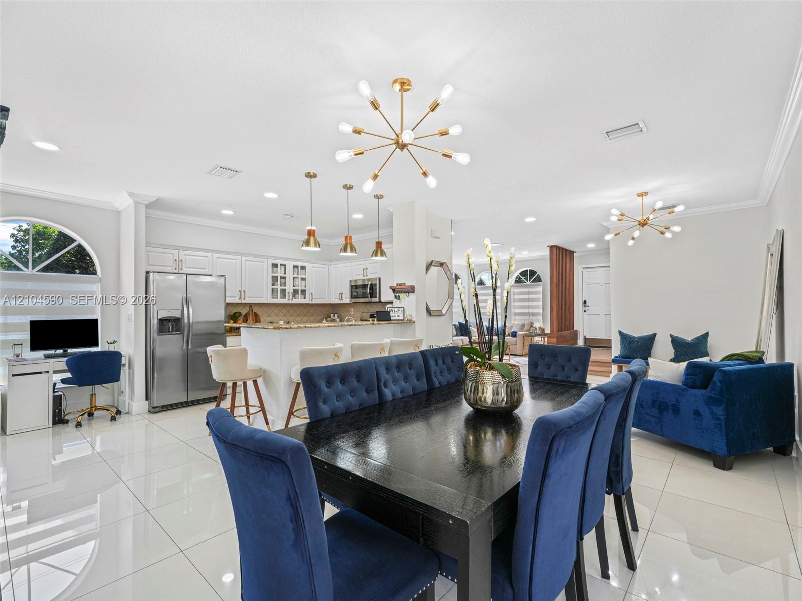 Open-concept area featuring polished tile flooring, contemporary multi-arm chandeliers, white cabinetry with integrated appliances, and an arched window Open-concept area featuring polished tile flooring, contemporary multi-arm chandeliers, white cabinetry with integrated appliances, and an arched window