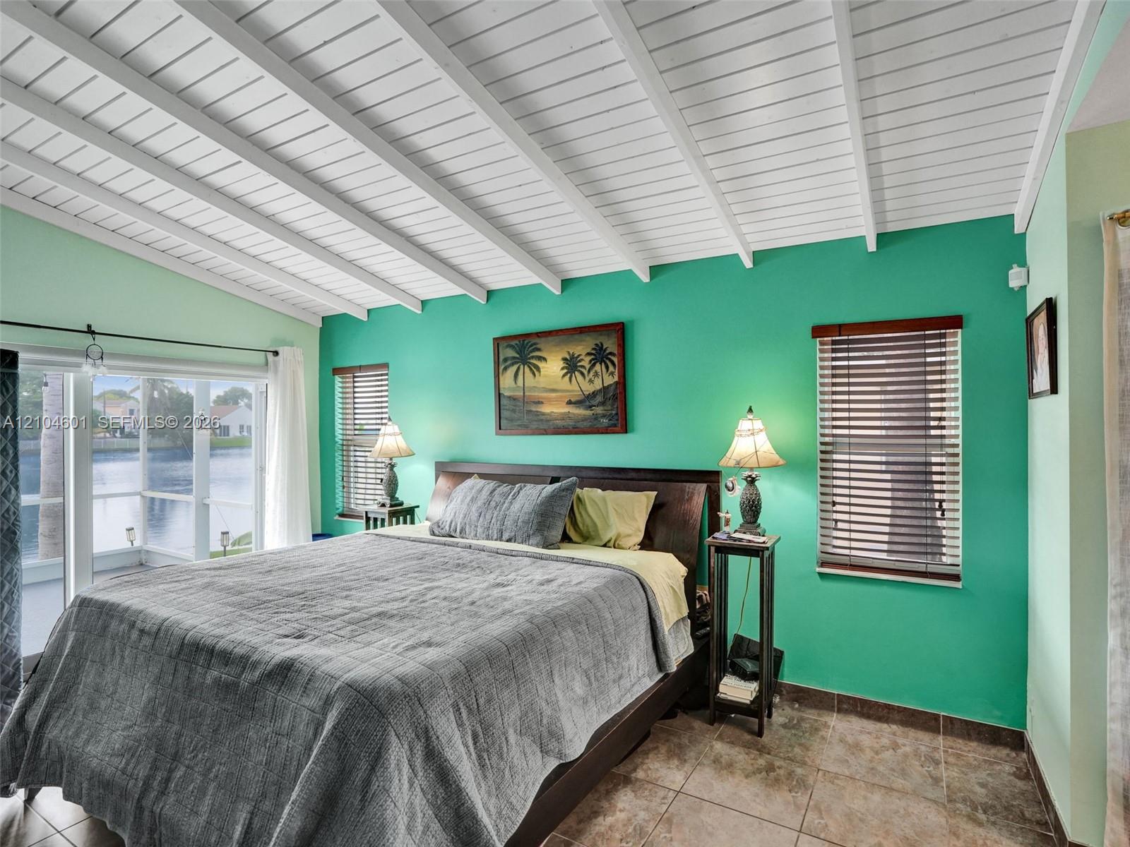Vaulted ceiling with exposed white beams, tile flooring, and multiple windows with horizontal blinds