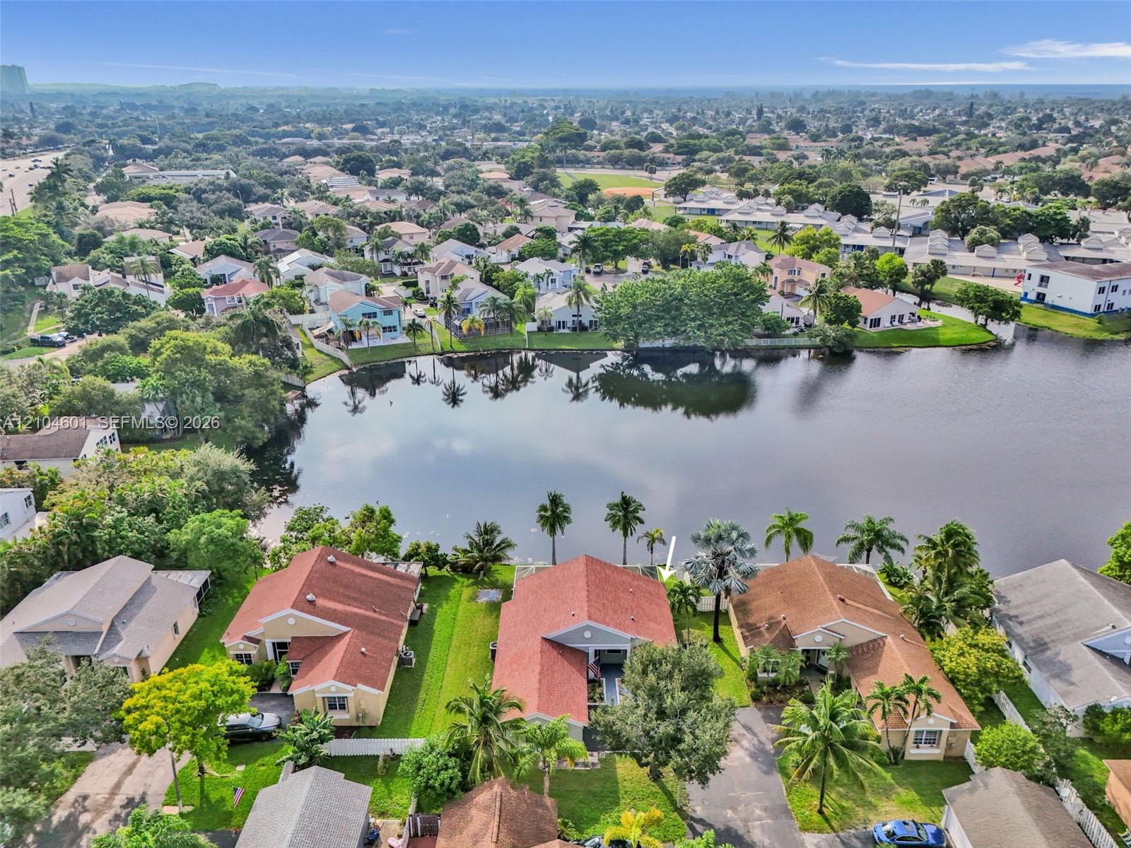 Aerial perspective featuring a waterfront property with a gable-roofed residence, mature palm trees, and rear yard access to the lake