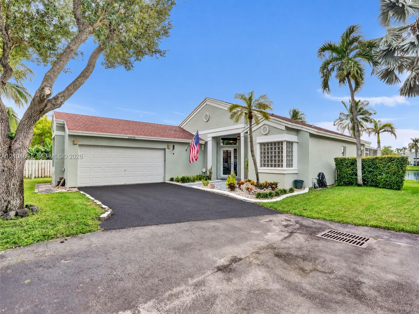 Single-story exterior featuring a shingled roof, glass block window accents, multi-car garage, and established landscaping