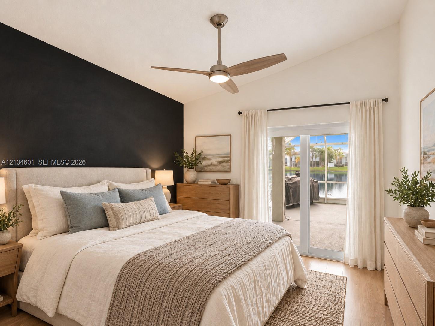 Vaulted ceiling featuring a central brushed-nickel LED ceiling fan and contrasting black accent wall, paired with sliding glass doors leading to a screened-in patio