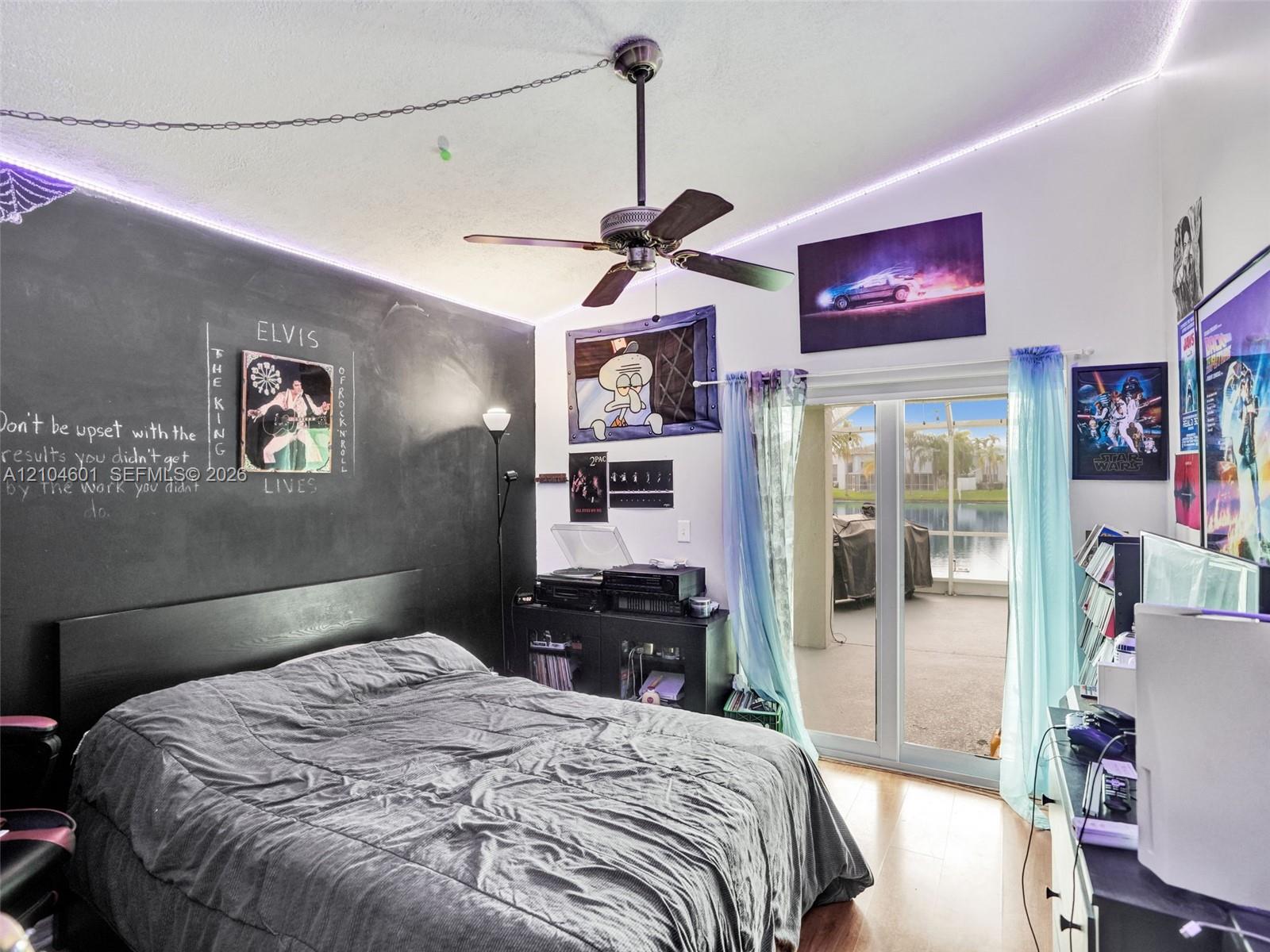 Vaulted ceiling with a central paddle fan, wood-finish flooring, and glass sliding doors providing exterior access
