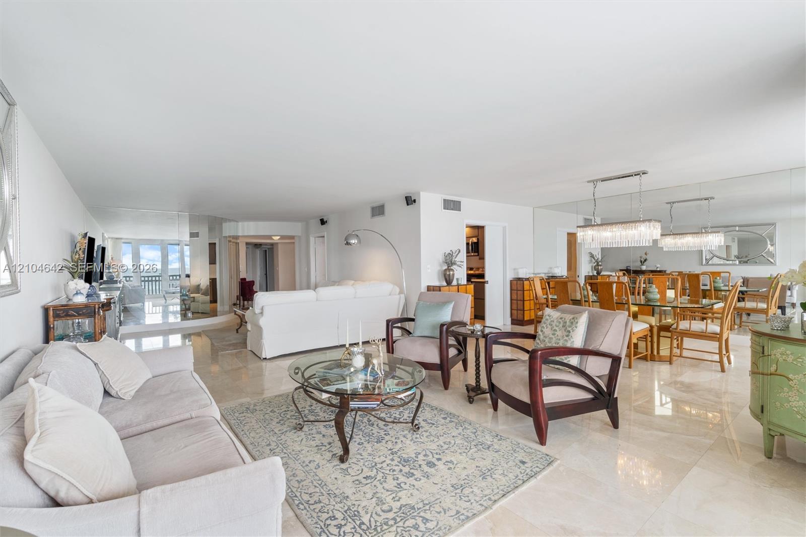 Open-concept interior featuring light-toned stone tile flooring, floor-to-ceiling wall mirror, and crystal-accented linear chandeliers