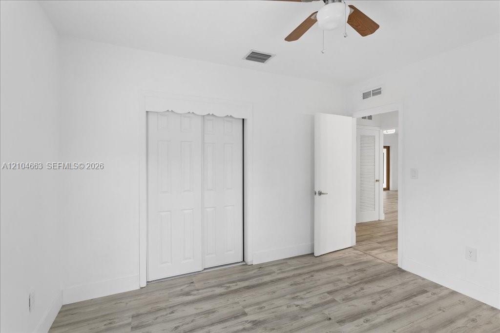 Room featuring wood-finish flooring, a ceiling fan with integrated lighting, and a dual-panel sliding closet door