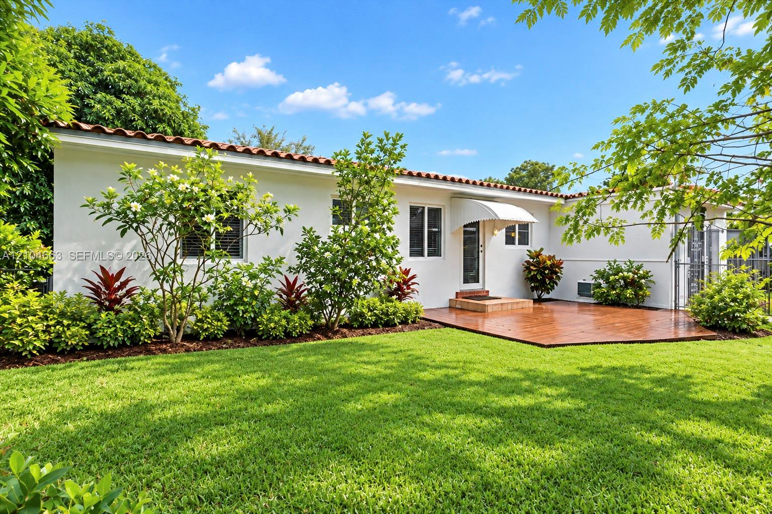 Stucco exterior featuring a terracotta tile roof, manicured lawn, stamped concrete patio, and mature landscaping