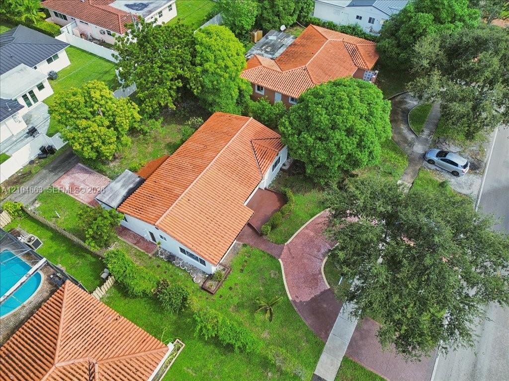 Aerial perspective of a residence featuring a terracotta-tile roof, paved circular driveway, and established canopy trees across the landscaped grounds