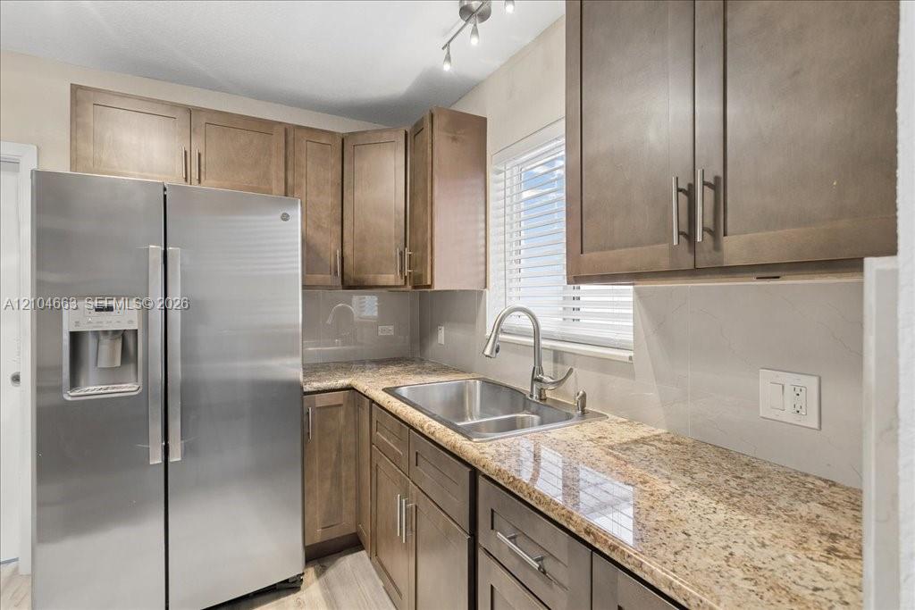 Kitchen featuring shaker-style cabinetry, stone countertops, stainless steel side-by-side refrigerator, stainless steel dual-basin sink with a gooseneck faucet, and track lighting Kitchen featuring shaker-style cabinetry, stone countertops, stainless steel side-by-side refrigerator, stainless steel dual-basin sink with a gooseneck faucet, and track lighting