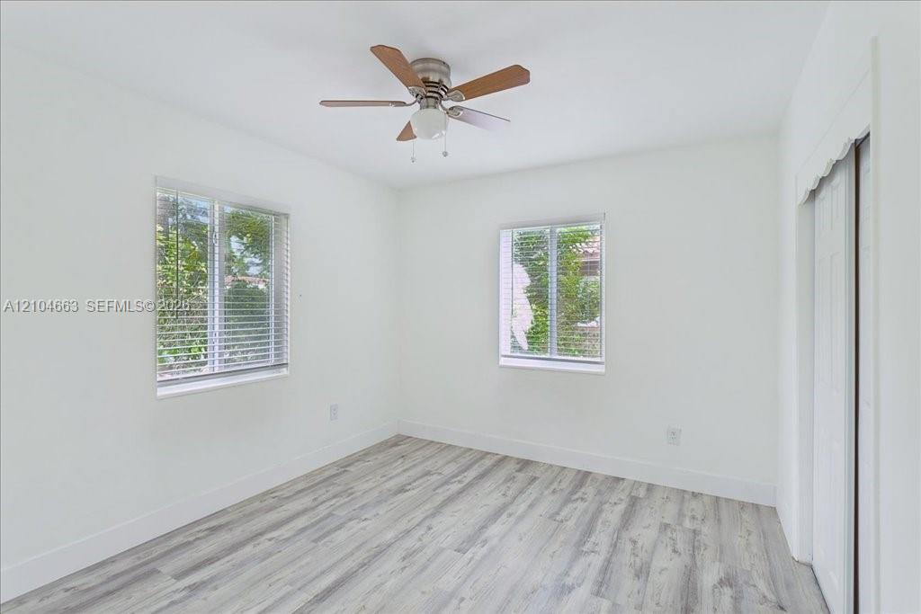 Neutral-toned room featuring wood-finish flooring, two windows with horizontal blinds, a ceiling fan with light fixture, and a sliding-door closet