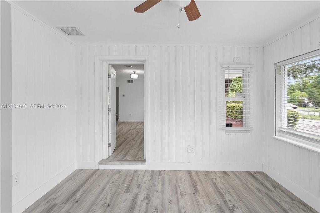 Room interior featuring wood-finish flooring, vertical panel wall detailing, and a ceiling fan