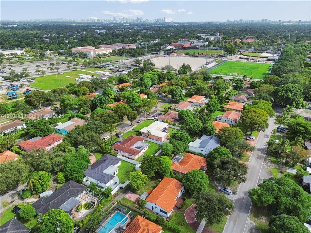 Aerial perspective of a residential neighborhood featuring mature canopy trees, tiled roofing, green space, and hardscape pathways