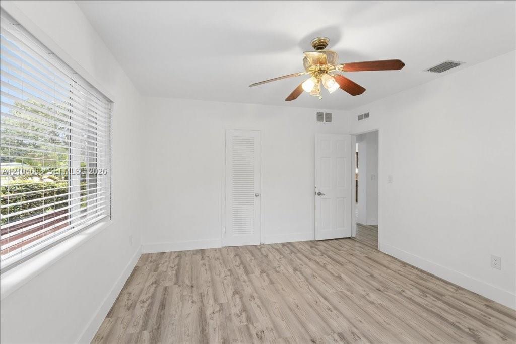 Interior room featuring wood-finish flooring, a multi-blade ceiling fan with integrated lighting, horizontal window blinds, and louvered closet doors Interior room featuring wood-finish flooring, a multi-blade ceiling fan with integrated lighting, horizontal window blinds, and louvered closet doors