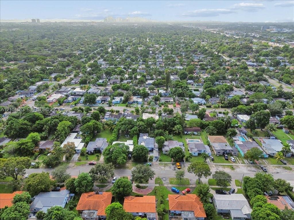 Aerial perspective of a residential neighborhood featuring mature tree canopy and city skyline backdrop