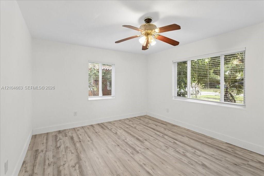 Room featuring wood-finish flooring, white walls, two multi-pane windows with horizontal blinds, and a central ceiling fan with integrated lighting Room featuring wood-finish flooring, white walls, two multi-pane windows with horizontal blinds, and a central ceiling fan with integrated lighting
