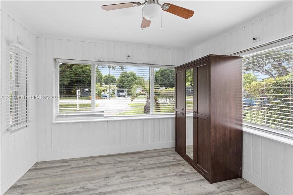 Room featuring wood-finish flooring, vertical plank wall paneling, large windows with horizontal blinds, and a ceiling fan with integrated lighting
