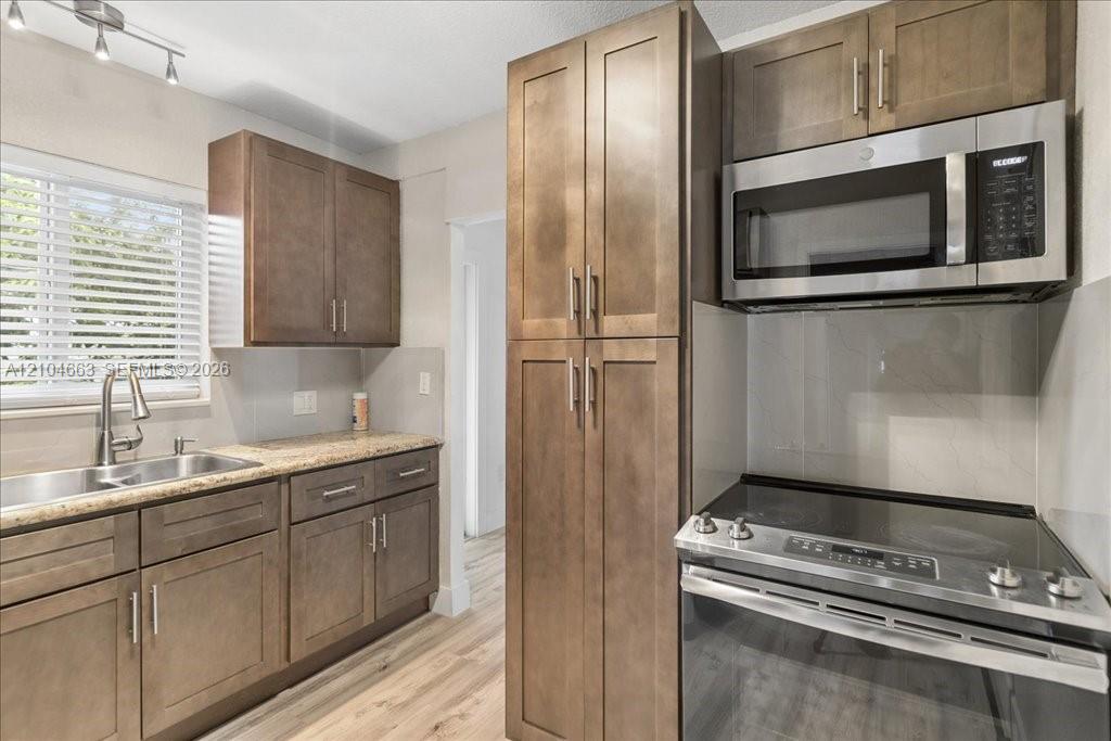 Kitchen featuring wood-finish cabinetry, stone-surface countertops, stainless steel appliances, and integrated track lighting Kitchen featuring wood-finish cabinetry, stone-surface countertops, stainless steel appliances, and integrated track lighting
