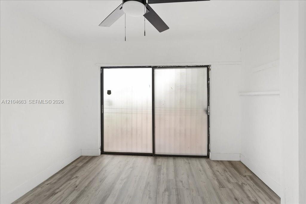 Room featuring wood-finish flooring, sliding glass door, and a ceiling-mounted light fixture with a fan Room featuring wood-finish flooring, sliding glass door, and a ceiling-mounted light fixture with a fan
