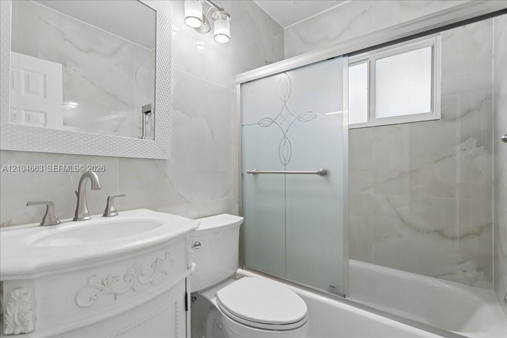 Bathroom featuring vanity with ornate detailing, wall-mounted mirror, sliding shower door with decorative etching, and large-format tile surround