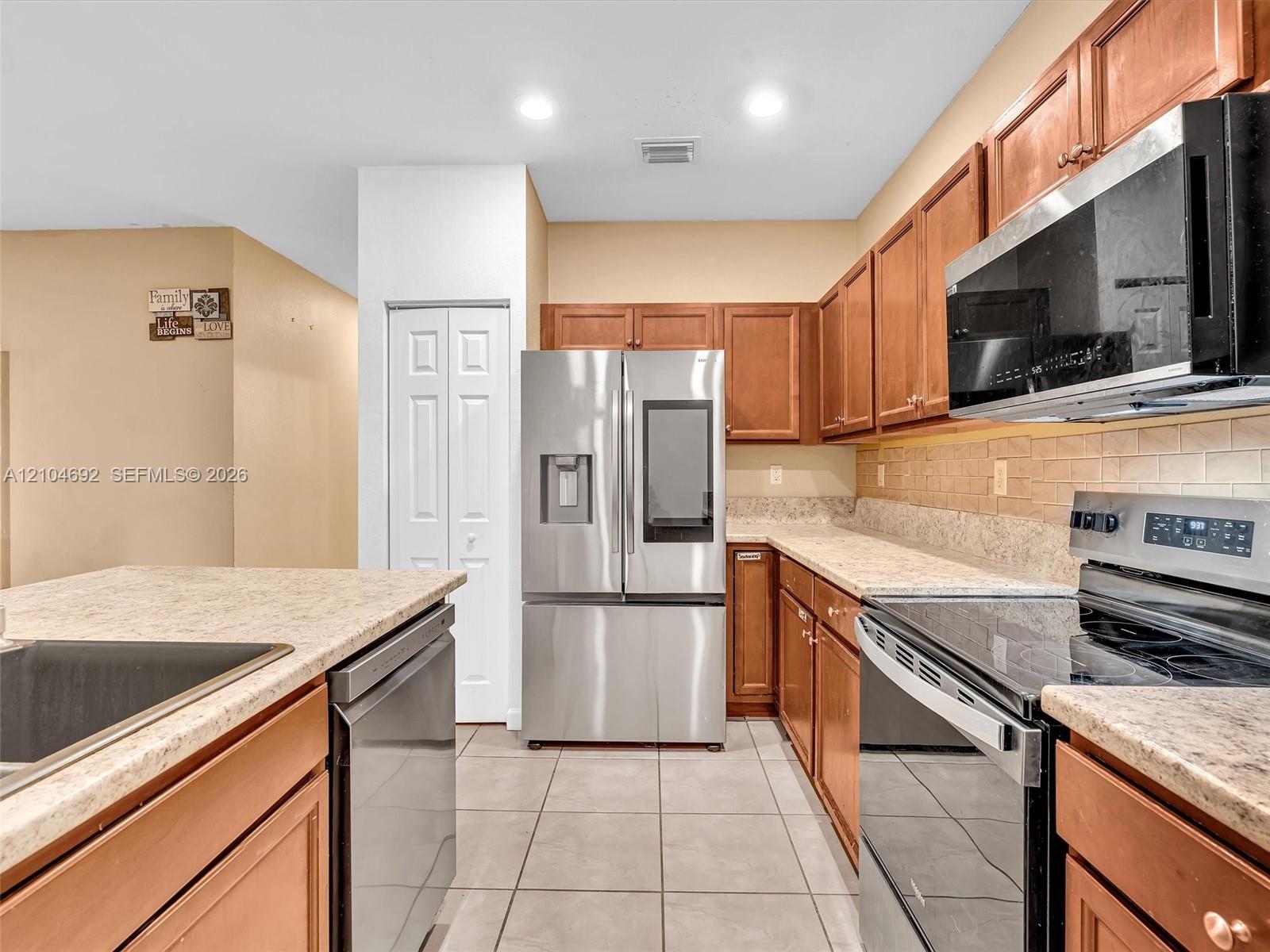 Kitchen featuring warm-toned wood cabinetry, neutral countertops, tile flooring, and integrated stainless steel appliances Kitchen featuring warm-toned wood cabinetry, neutral countertops, tile flooring, and integrated stainless steel appliances