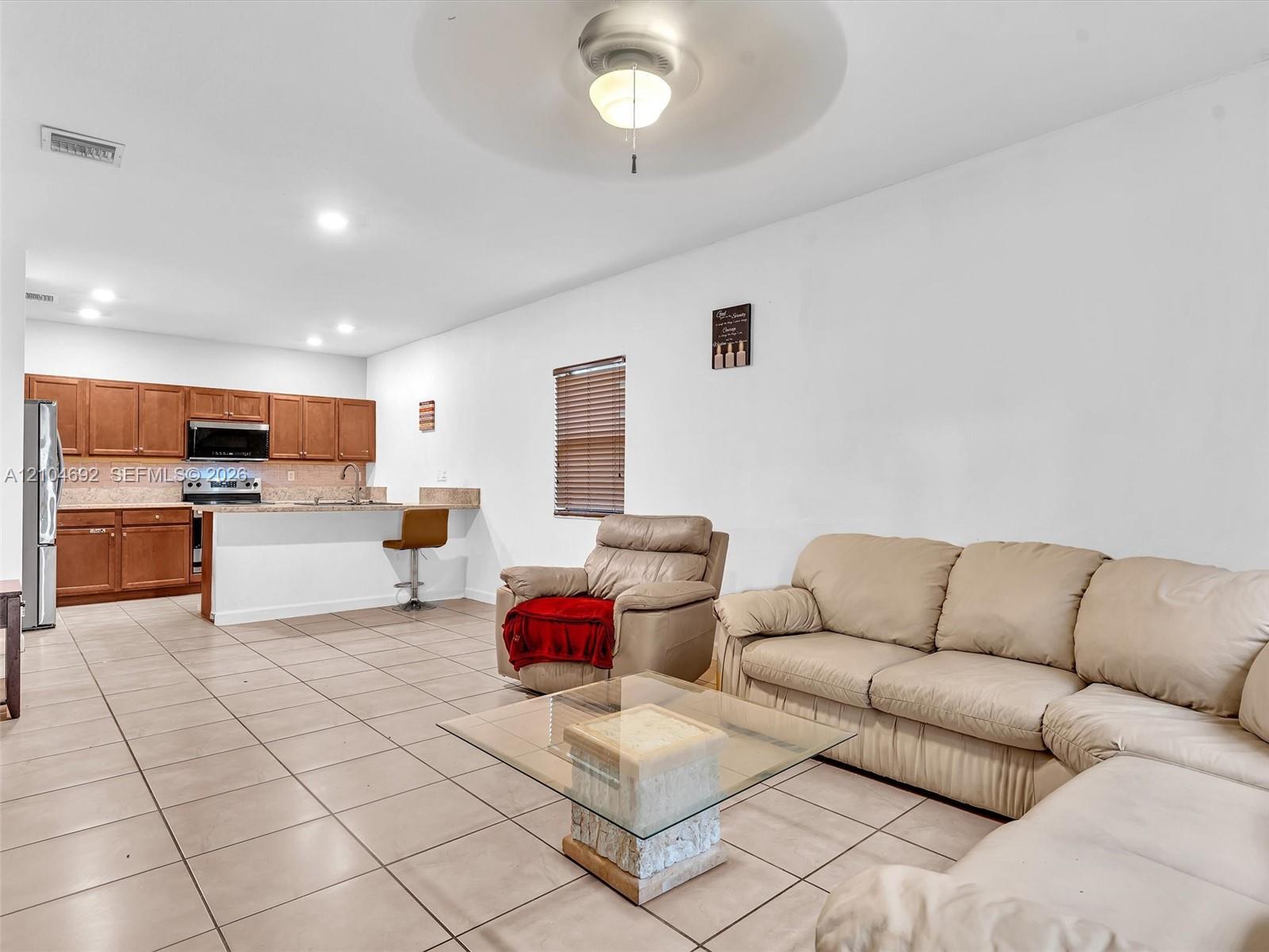 Open-concept interior featuring large-format tile flooring, wood cabinetry, stone countertops, a breakfast bar, and recessed lighting Open-concept interior featuring large-format tile flooring, wood cabinetry, stone countertops, a breakfast bar, and recessed lighting