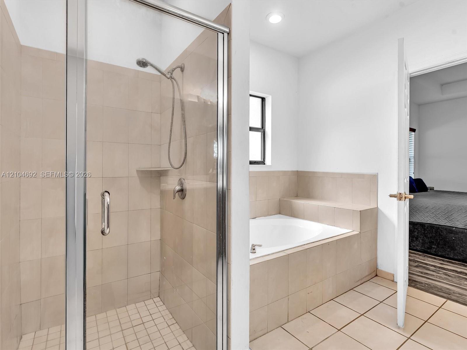 Shower enclosure featuring a glass door, neutral-toned wall tiles, a built-in recessed shelf, and a detachable showerhead, paired with a built-in soaking tub surrounded by matching tile finish