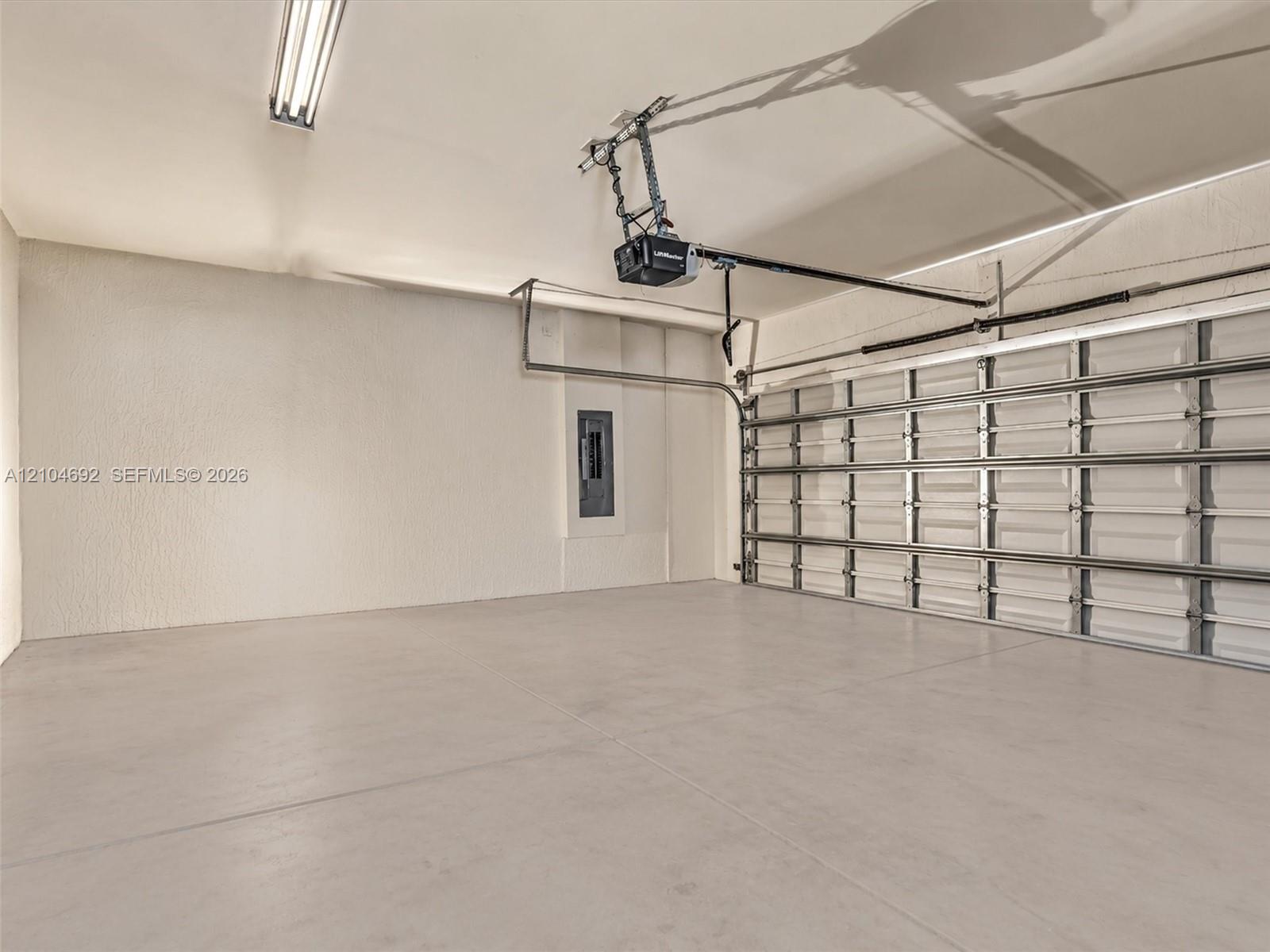 Finished garage interior featuring concrete flooring, textured walls, a multi-panel overhead door, and an integrated electrical service panel