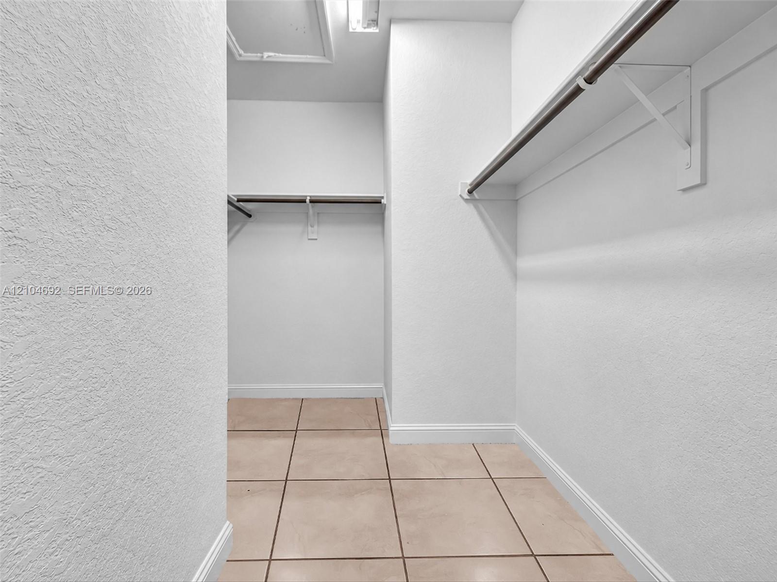 Walk-in closet featuring ceramic tile flooring, neutral textured wall finishes, and integrated shelving with metal hanging rods